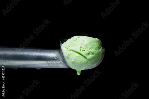 A metal spoon with a melting pistachio ice cream scoop dripping drops from it. Isolated on a black background.