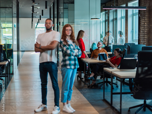 African-American businessman and his businesswoman colleague stand at the forefront with crossed arms, exuding confidence and leadership, while their diverse team diligently works behind them