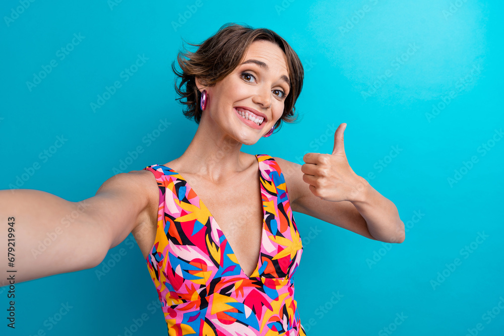 Fototapeta premium Photo of cheerful positive woman with bob hair dressed colorful clothes shwoing thumb up make selfie isolated on blue color background