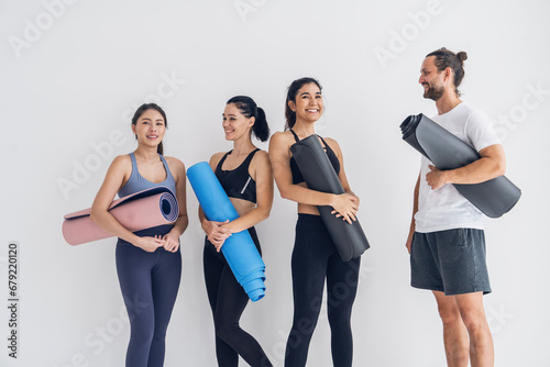 Group of three female friends and a man wearing exercise clothes holding yoga mats preparing to do yoga exercises together in studio.Healthy lifestyle concept