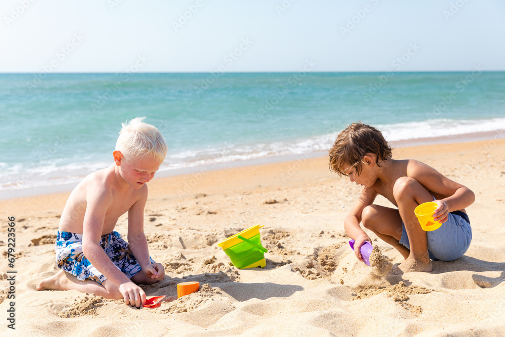 Children two little boys playing on the beach on summer holidays. Children having fun with a sand on the seashore. Vacation concept. Happy sunny day. Joyful children with beautiful sea, sand Children two little boys playing on the beach on summer holidays. Children having fun with a sand on the seashore. Vacation concept. Happy sunny day. Joyful children with beautiful sea, sand
