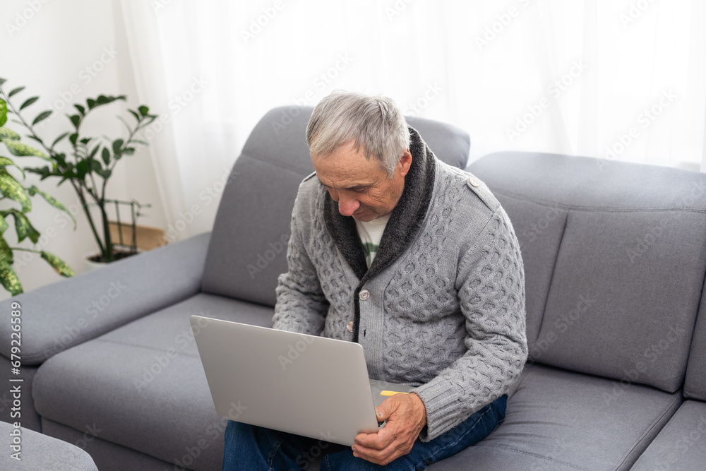 Older man sitting on sofa, smiling at computer screen at home