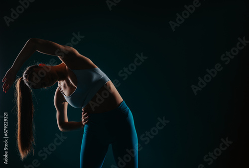 Confident woman showcasing body transformation through exercise in a dark studio. Muscular silhouette, fit physique, strong muscles. Fitness model inspiring others.