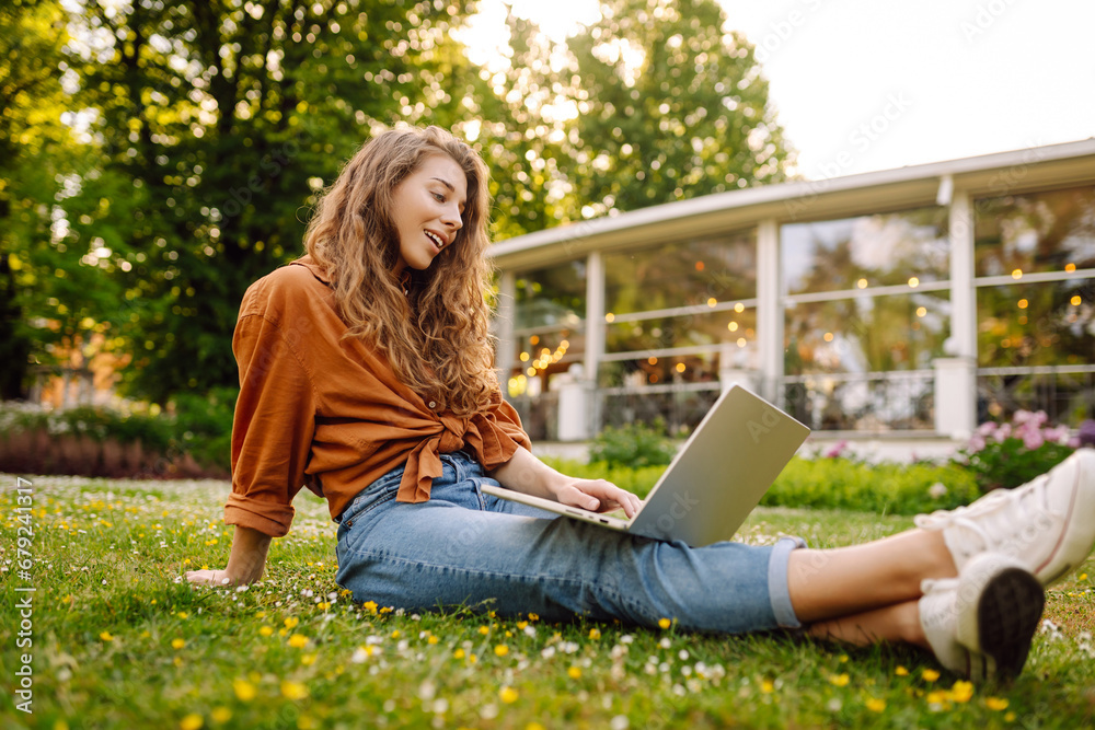 Beautiful woman in casual clothes on a green lawn with a laptop. Happy freelancer woman working on laptop outdoors. Education and freelancing concept. Beautiful woman in casual clothes on a green lawn with a laptop. Happy freelancer woman working on laptop outdoors. Education and freelancing concept.