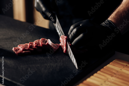 Close-up of a chef wearing black gloves expertly slicing meat, showcasing culinary precision and hygiene