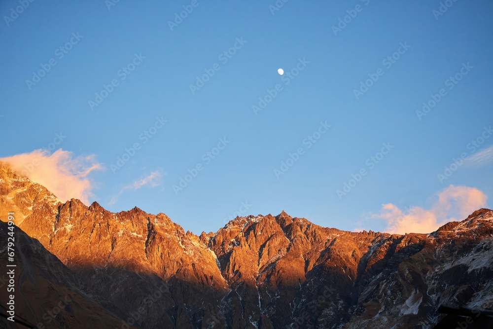 High mountains illuminated by the sun. Landscape at sunset. Moon over the mountains