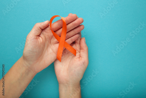 Hands holding orange color ribbon on blue background. Kidney Cancer Awareness, Leukemia disease, Skin cancer awareness, World Cancer Day. photo