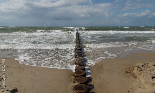 Holzpfosten in rauen Wellen an einem stürmischen Tag am Meer unter einem bewölkten Himmel.