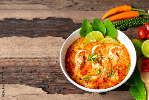 Obraz na plátně Tom Yum Goong or Shrimp soup spicy sour Soup Traditional food in Thailand contains chili, lime,lemongrass, lime leaf, along with cooked rice in a white dish on the old wood background from top view