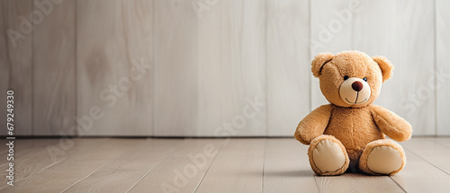 A funny teddy bear on the wooden floor of a room sitting near the wall. Simple, minimalist photograph, template with large copyspace