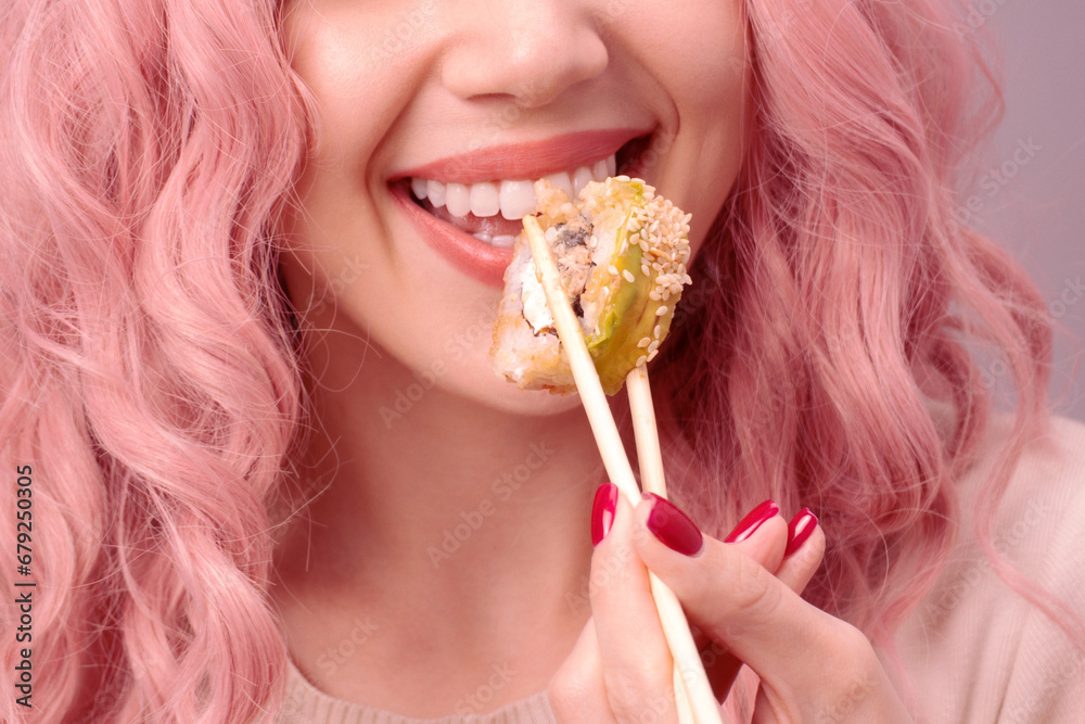 Young woman with red nails and pink hair is eating sushi. Young woman with red nails and pink hair is eating sushi.