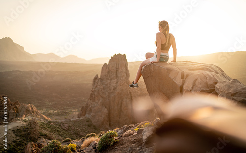 junge Wandererin sitzt auf einem großen Felsen und genießt den Sonnenuntergang