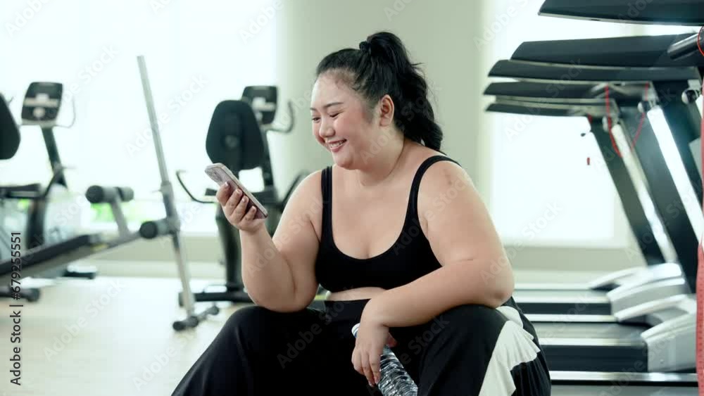 Happy Chubby woman sitting and resting after exercising in the fitness center Watch videos on social media on your smartphone. Enjoy movies. Cute Asian overweight woman trying to lose weight Happy Chubby woman sitting and resting after exercising in the fitness center Watch videos on social media on your smartphone. Enjoy movies. Cute Asian overweight woman trying to lose weight