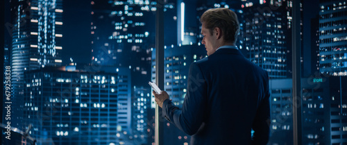 Tableau sur toile Backview of Handsome Caucasian Businessman in Stylish Suit Standing Next to Window in Big City Office with Skyscrapers Late At Night