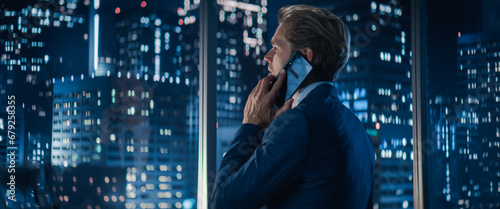 Konstfotografi Backview of Handsome Caucasian Businessman in Stylish Suit Standing Next to Window in Big City Office with Skyscrapers Late At Night
