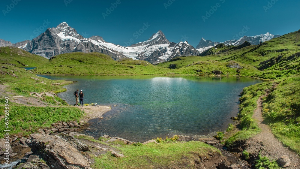 Scenic view of two hikers at a lake in Swiss snow-capped mountains