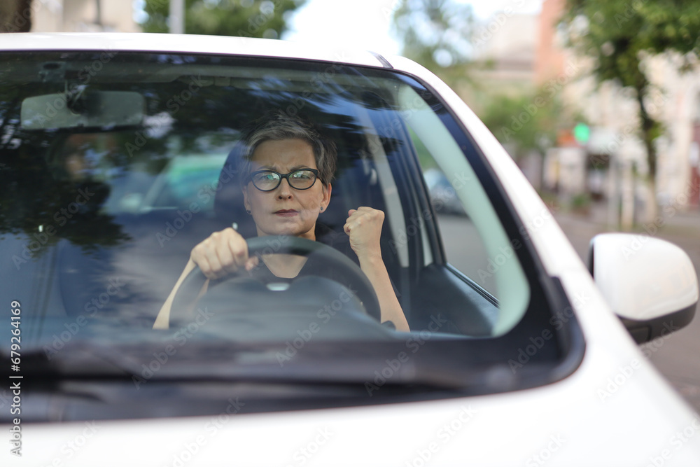 An angry and frustrated mature woman driving a car, expressing fury and stress in a portrait, despite a successful and confident demeanor.