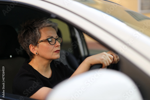 A serious and confident mature woman behind the wheel, embodying a mix of joy, safety, and a modern lifestyle in her car.