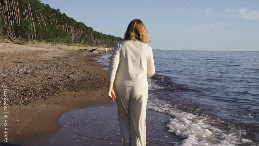 A happy woman skips barefoot along the seashore in the water. In the background there is a beach and a forest. A happy woman skips barefoot along the seashore in the water. In the background there is a beach and a forest.