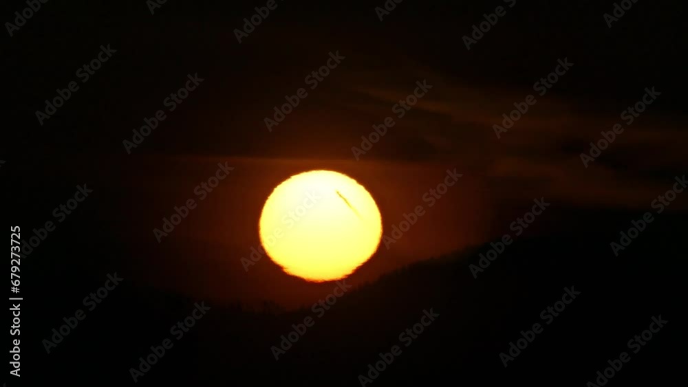 Dark sky and yellow sun during sunrise over horizon of mountains with forests. Sun disc with Atmospheric refraction, distorted shape of sphere caused by atmospheric optical phenomenon - timelapse. Dark sky and yellow sun during sunrise over horizon of mountains with forests. Sun disc with Atmospheric refraction, distorted shape of sphere caused by atmospheric optical phenomenon - timelapse.