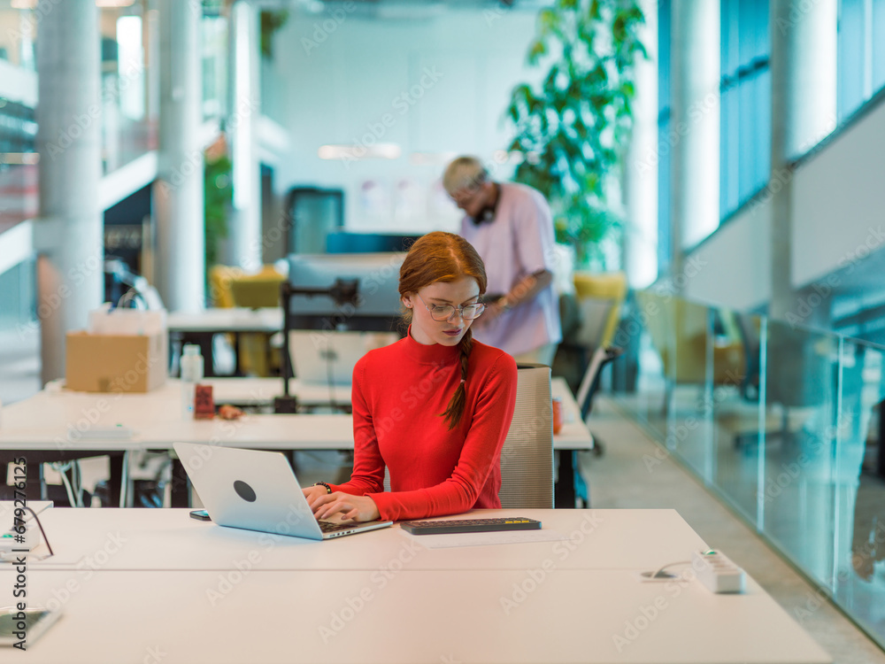 In a modern startup office, a professional businesswoman with orange hair sitting at her laptop, epitomizing innovation and productivity in her contemporary workspace