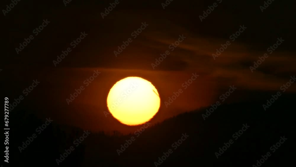 Dark sky and yellow sun during sunrise over horizon of mountains with forests. Sun disc with Atmospheric refraction, distorted shape of sphere caused by atmospheric optical phenomenon - real time. Dark sky and yellow sun during sunrise over horizon of mountains with forests. Sun disc with Atmospheric refraction, distorted shape of sphere caused by atmospheric optical phenomenon - real time.