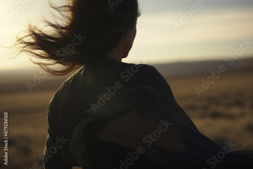 A solitary woman stands amidst a vast desert landscape, captured in full focus against a backdrop of windswept sands.