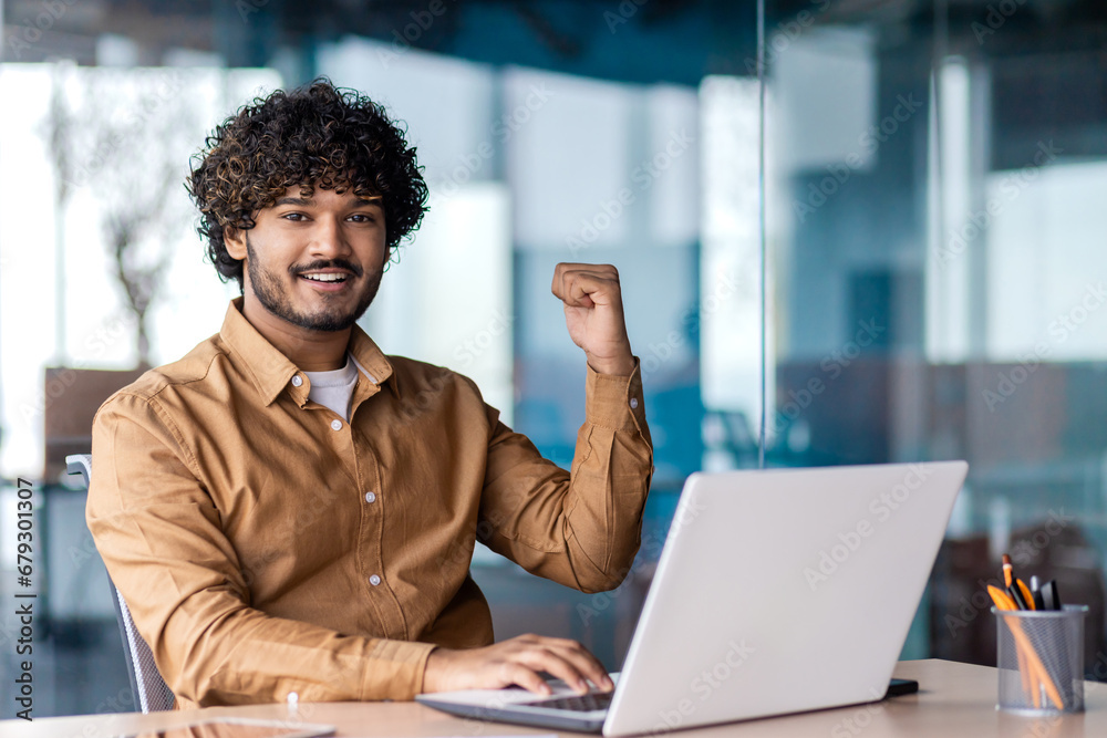 Portrait of winner businessman at workplace, smiling man celebrating successful achievement results and looking at camera, holding hands up victoriously. Portrait of winner businessman at workplace, smiling man celebrating successful achievement results and looking at camera, holding hands up victoriously.