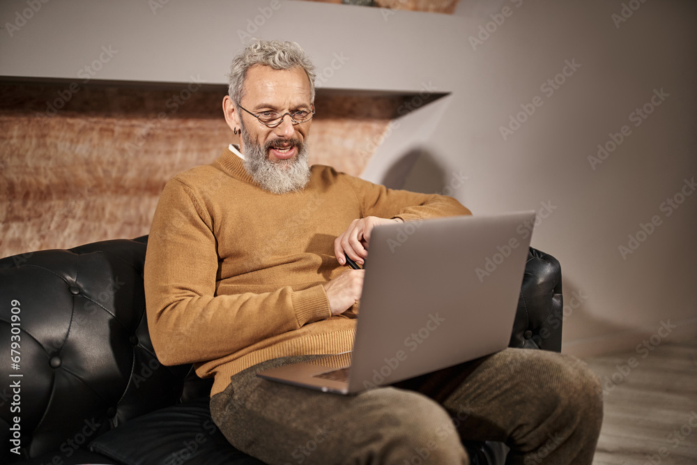 joyful middle aged psychologist with beard laughing during online consultation with client on laptop