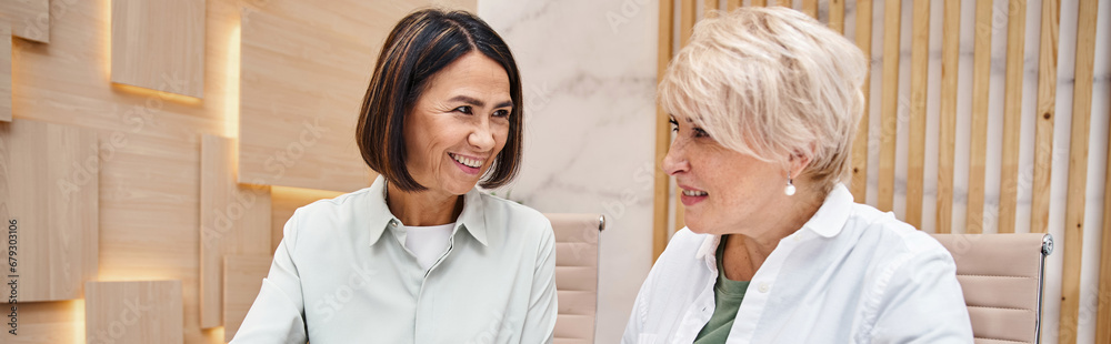 happy middle aged lesbian couple in smart casual attire smiling in real estate office, banner happy middle aged lesbian couple in smart casual attire smiling in real estate office, banner