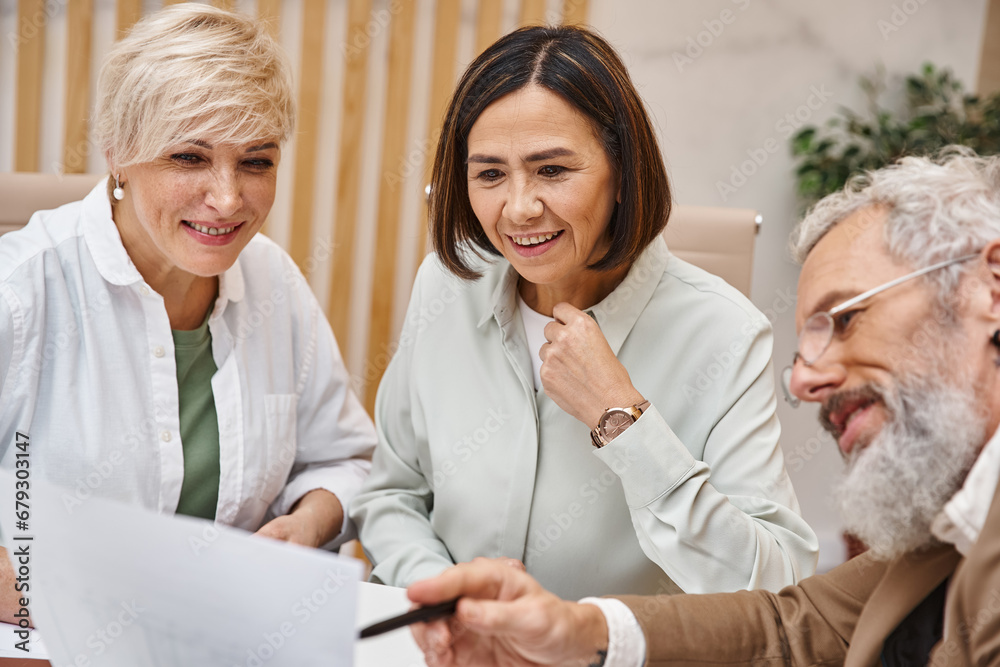 Obraz premium middle aged bearded realtor showing contract to lesbian couple in real estate office, lgbt couple