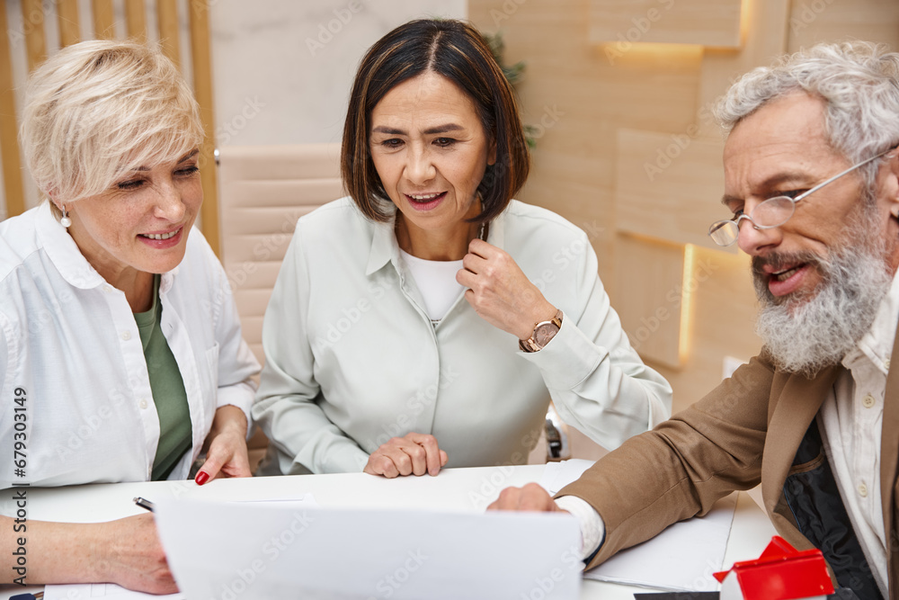 Obraz premium middle aged bearded realtor showing contract to lesbian couple in real estate office, lgbt couple