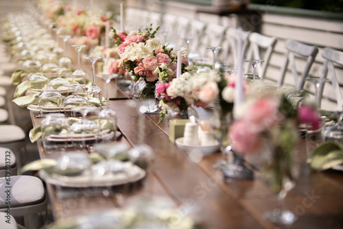 A large  long  decorated  wooden table and chairs  covered with a white tablecloth with dishes  flowers  candles.
