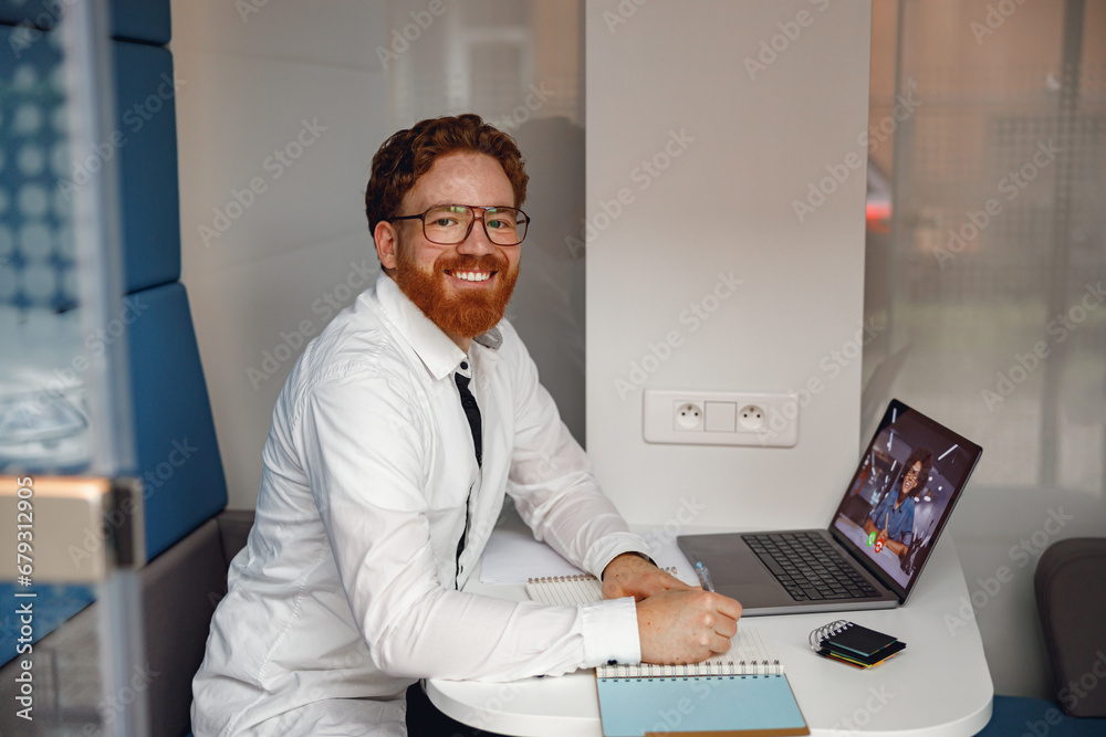 Businessman have online meeting with colleague and making notes while sitting in cozy coworking