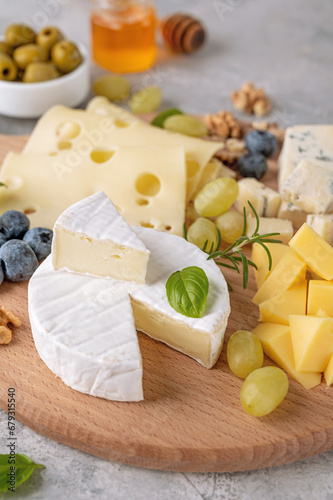 Cheese plate with a variety of cheeses, honey, grapes, nuts, olives, blueberries and fresh herbs on a concrete background. A festive snack. Top view, copy space