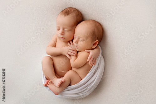 Tiny newborn twins boys in white cocoons on a white background. A newborn twin sleeps next to his brother. Newborn two twins boys hugging each other. Professional studio photography. 