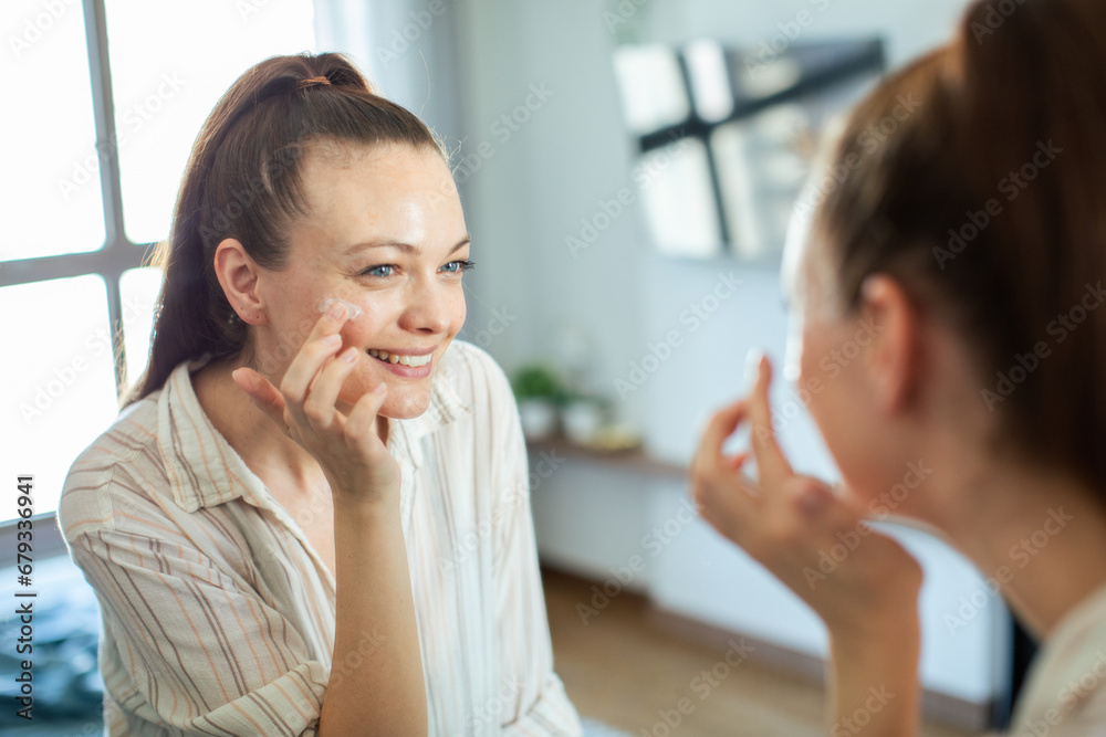 Smiling Woman Applying Facial Cream in Front of Mirror at Home Smiling Woman Applying Facial Cream in Front of Mirror at Home