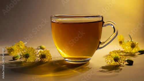 Uma xícara com chá sobre superfície amarela com flores e iluminação vinda da lateral.
