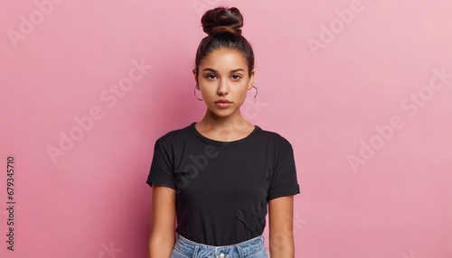 serious displeased latin woman with hair bun raises eyebrows looks attentively at camera purses lips has dimple on cheek dressed in casual black t shirt and jeans isolated over pink background photo