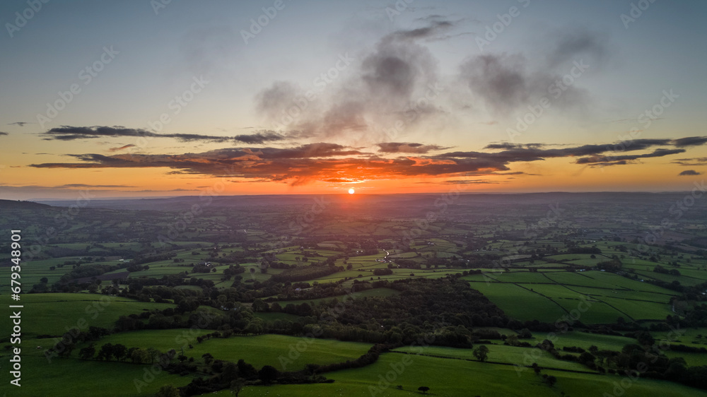 Fototapeta premium view of the sunrise above the lush green Wye Valley in South Wales shot from the trig point of the Skirrid Fawr in Abergavenny