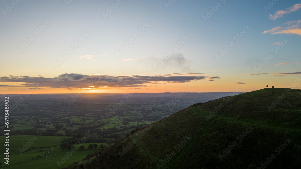 The sun rises over the Skirrid Fawr mountain near Abergavenny in the Brecon Beacons Black Mountains national park. morning walkers enjoy rugged natural beauty in Bannau Brycheiniog South Wales