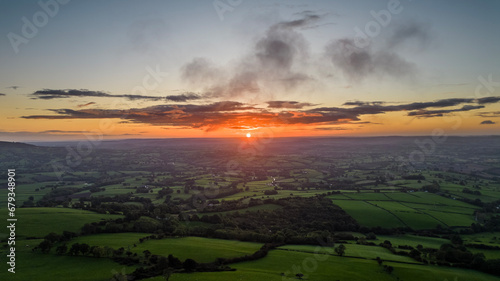 view of the sunrise above the lush green Wye Valley in South Wales shot from the trig point of the Skirrid Fawr in Abergavenny