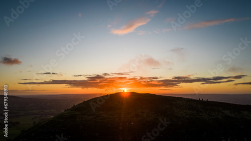 The sun rises over the Skirrid Fawr mountain near Abergavenny in the Brecon Beacons Black Mountains national park. morning walkers enjoy rugged natural beauty in Bannau Brycheiniog South Wales