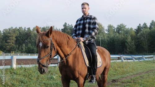 Young man riding a horse. Farmer on horseback. A man riding a horse. Outdoor stable. Non-professional rider holding the reins