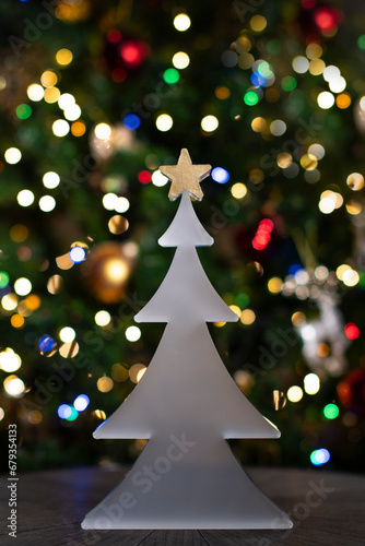 Sapin en verre blanc avec son étoile dorée de Noël devant des décoration lumineuse et colorés de rouge, vert, blanc  de Noël 