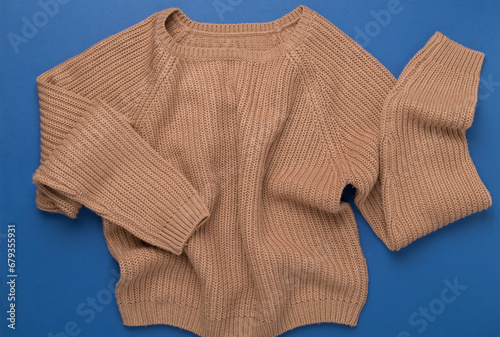 Beige knitted sweater on color background, top view