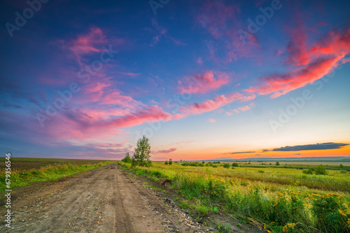 Rural landscape with ground road in a countryside at summer sunset