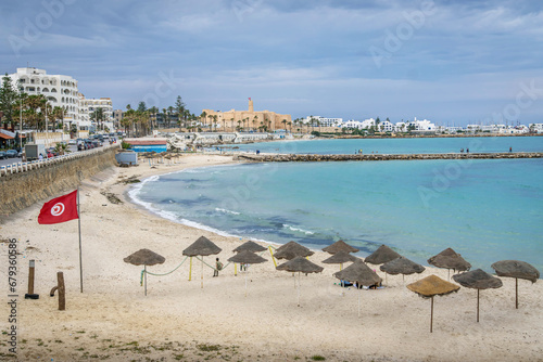 Fotografie The beach and Mediterranean sea coastline at resort town of Monastir, Tunisia, with the long pier, Tunisian flag, umbrellas, waterfront, and Raban (castle) at old town at the background