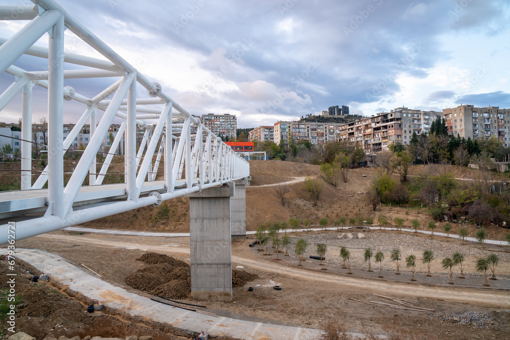 Iron pedestrian bridge over a small canyon painted in white. Tbilisi