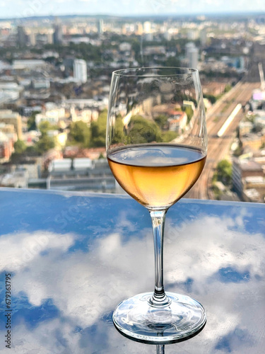 Glass of chilled rose wine on a table in a restauarnt overlooking a city. The sky and clouds are reflected in the table top.No people. photo